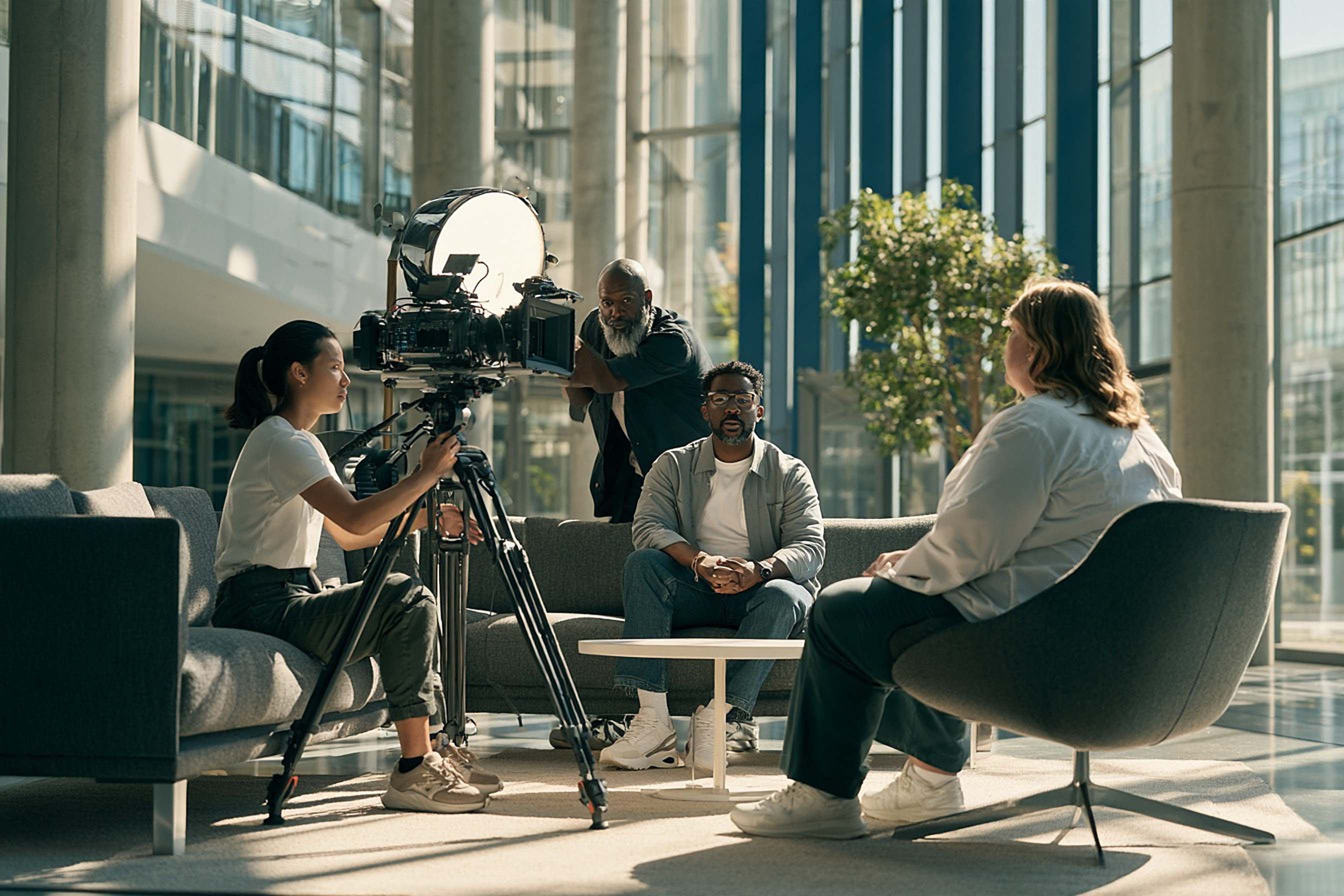 A small crew films a corporate interview in a bright modern atrium.