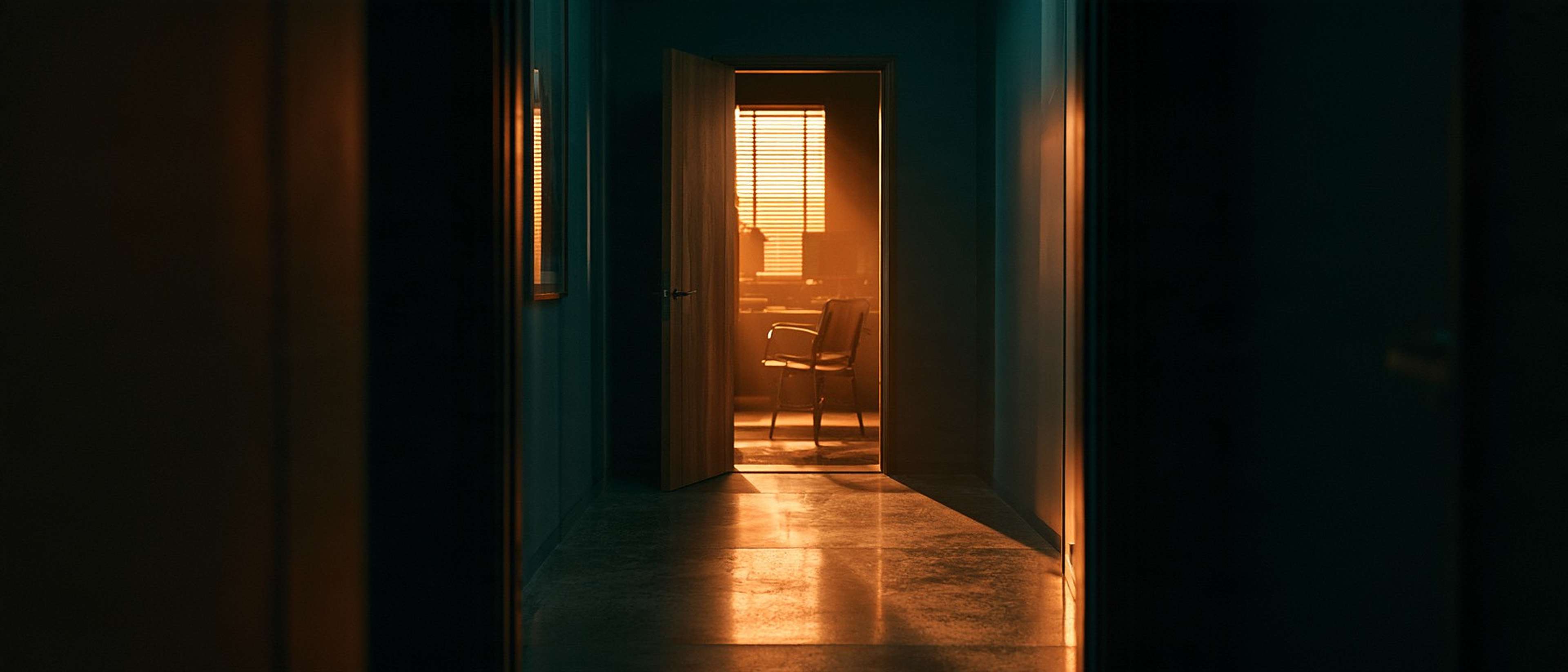 Warm morning light spills through an open door at the end of a dark studio corridor.