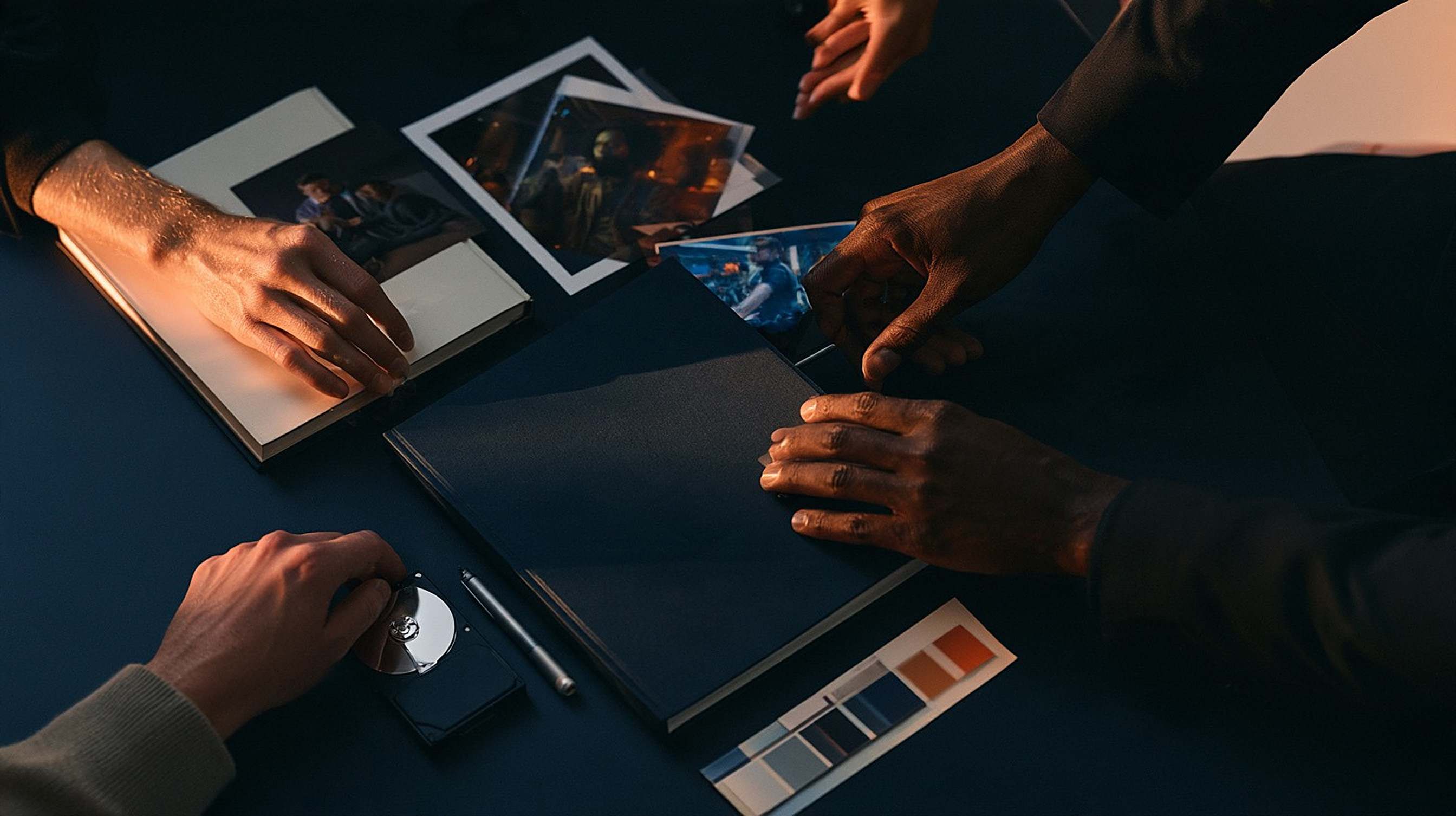Hands pass a prepared project brief, stills and a colour strip across a dark desk.